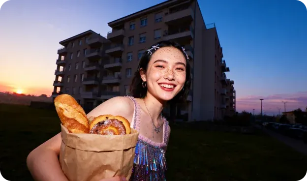 Social Campaigns — Freckled girl in a sequined top hugging a paper bag of bread under a dusk sky